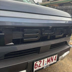Glossy black BYD emblem integrated into a sleek grey car front grille.