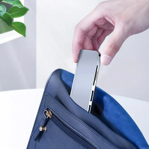 Hand placing a sleek silver metallic power bank into a professional navy blue leather bag.