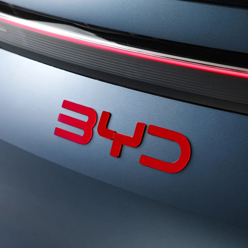 Close-up of a red metallic BYD emblem on a sleek grey car body.