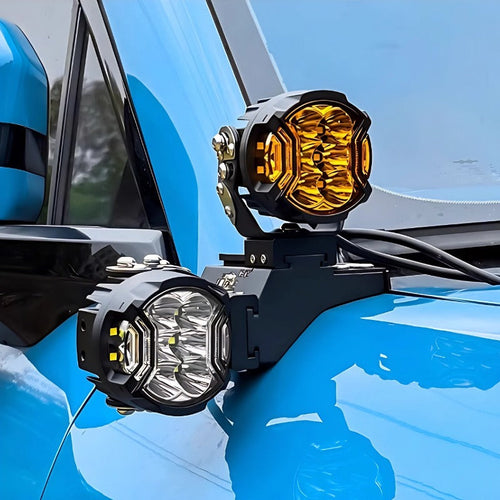 Black metal mounted amber and clear LED auxiliary driving lights on a blue vehicle.