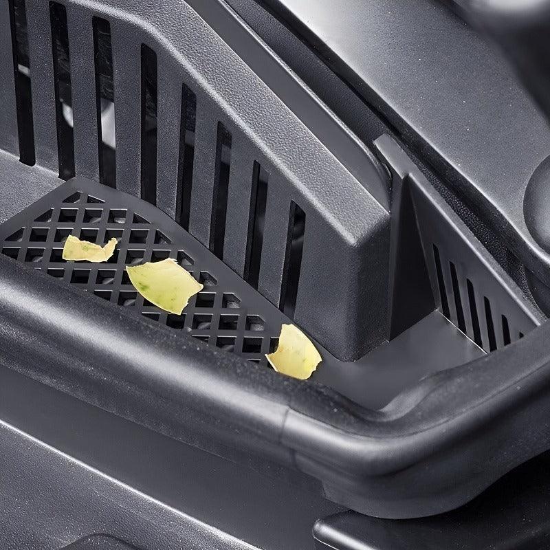 Close-up of a black durable plastic car floor mat with food crumbs on its textured surface.