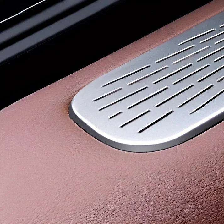 Silver metallic slotted trim piece on premium brown textured leather car interior.
