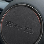 Black textured leather steering wheel cover with red trim and embossed BYD logo.