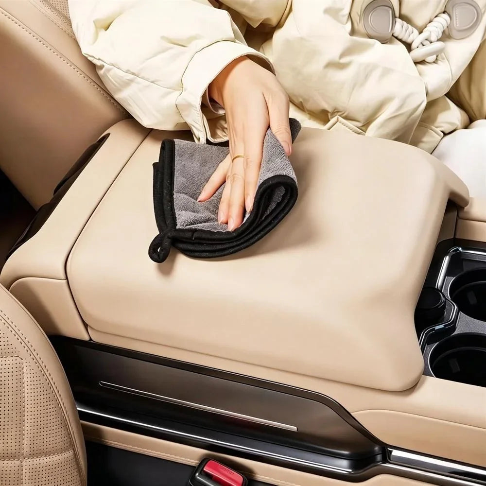 Hand cleaning a beige leather car center console with a grey microfiber cloth.