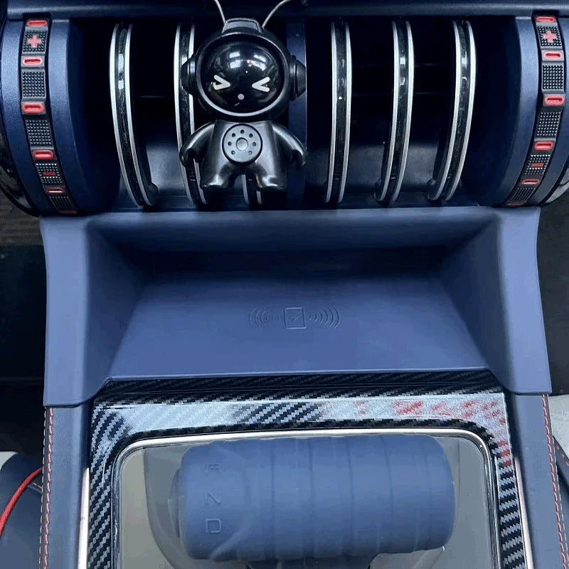 Blue carbon fiber texture center console with wireless charging pad and astronaut ornament.