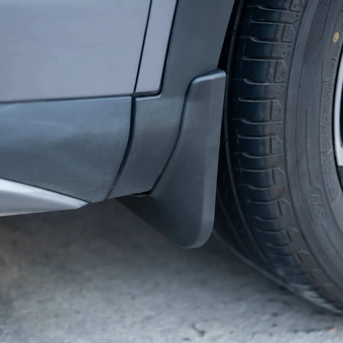 Durable matte black ABS plastic mud flap installed on a grey vehicle wheel arch.