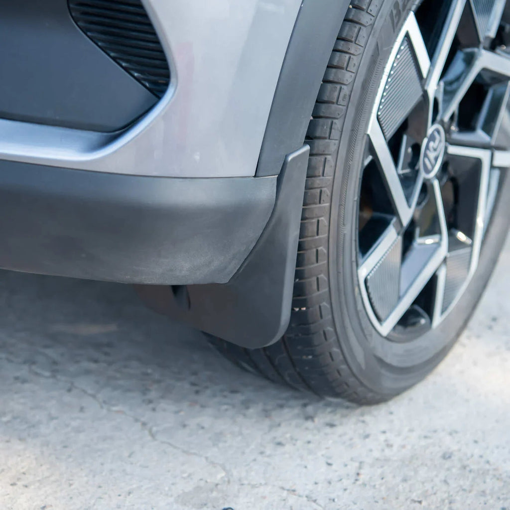 Durable matte black rubber mud flap installed behind the front wheel of a grey car.