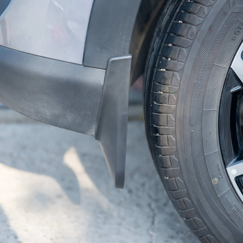Black durable rubber mud flap installed on the side of a grey car near the tire.
