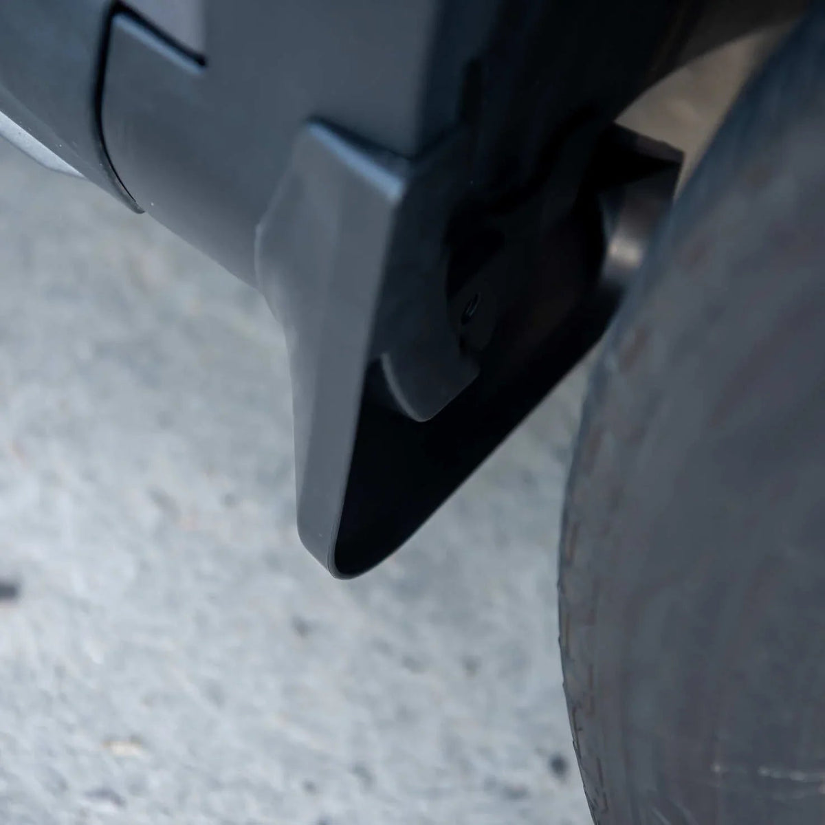 Durable matte black plastic mud flap installed behind the vehicle wheel for splash protection.