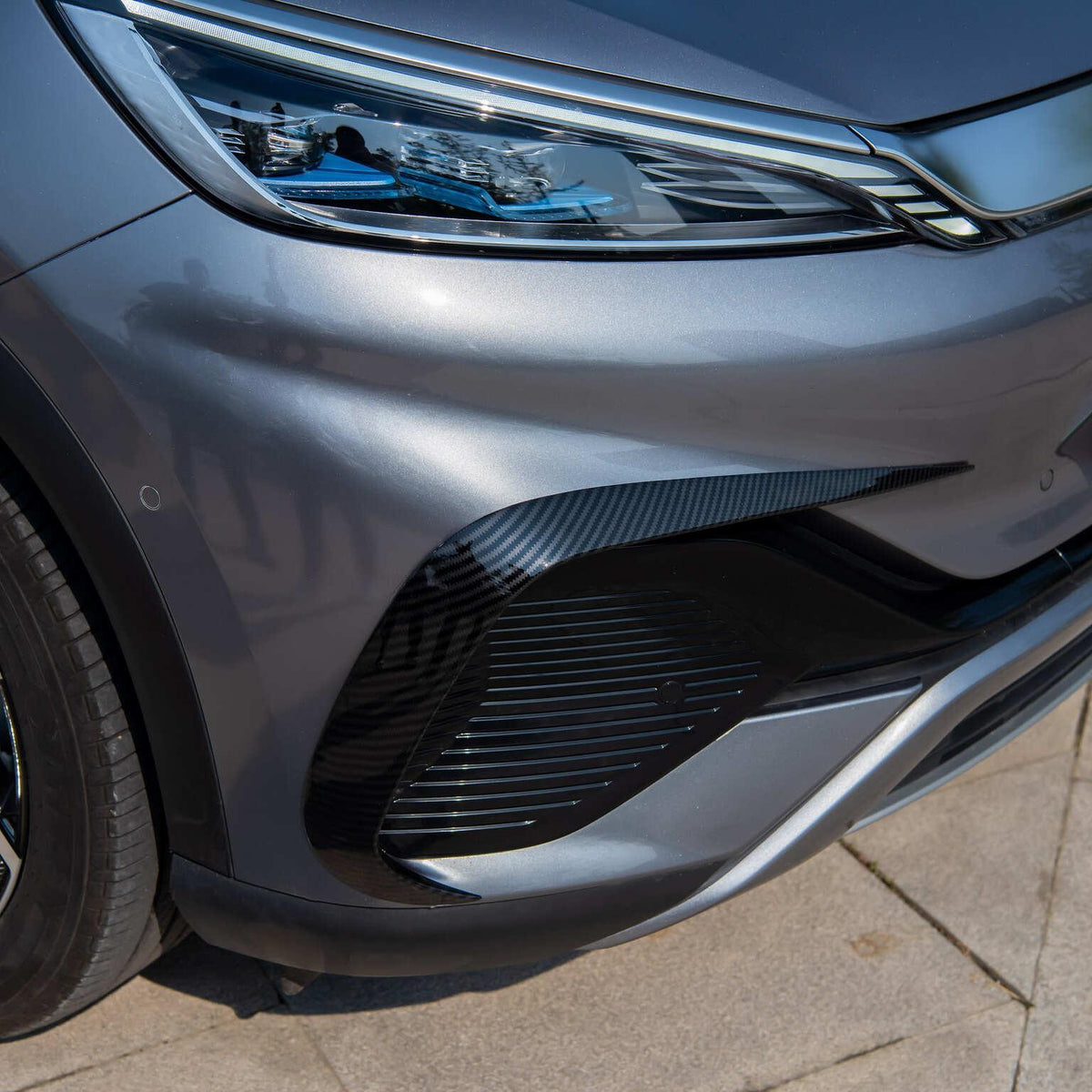 Close-up of a grey car featuring a carbon fiber front bumper trim accessory.