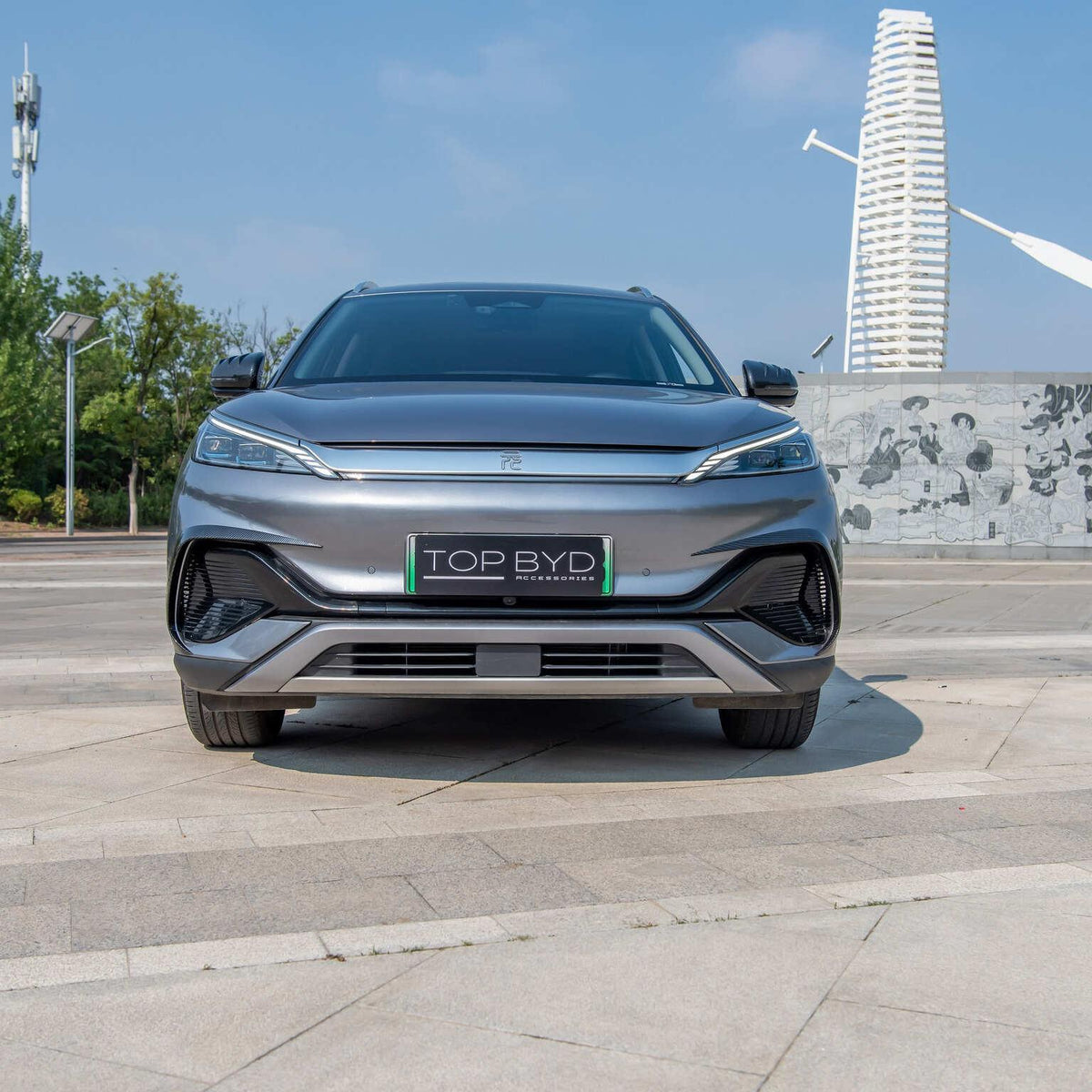 Front view of a sleek metallic grey BYD electric car parked on a paved urban plaza.