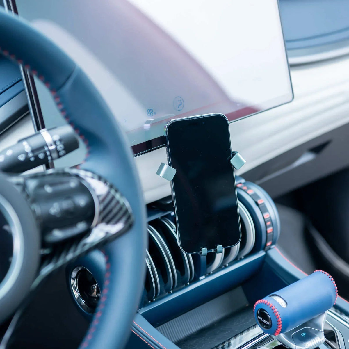 Black sleek smartphone mounted on a minimalist dashboard holder in a blue leather interior.