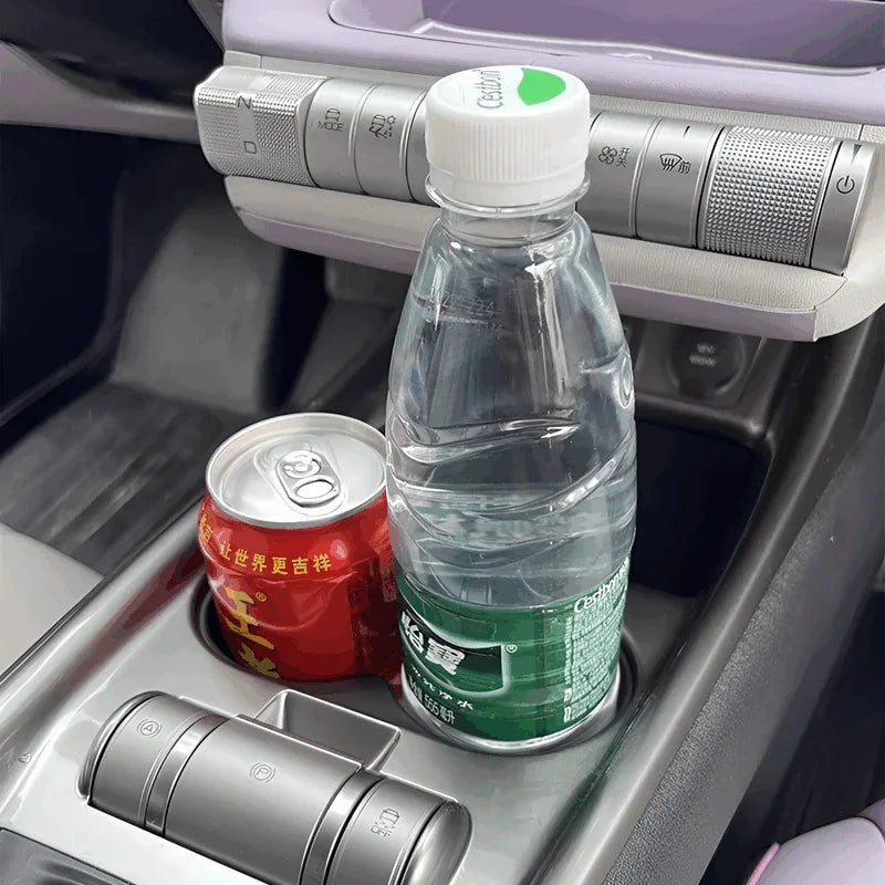 Clear plastic water bottle and red aluminum soda can placed in a grey car center console cup holder.