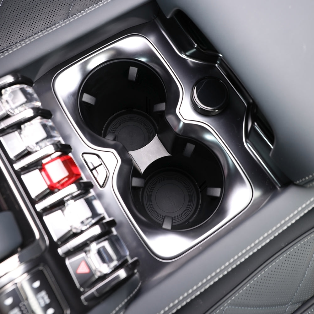 Close-up of a premium black glossy center console with dual cupholders and grey leather stitching.
