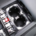 Close-up of a premium black glossy center console with dual cupholders and grey leather stitching.