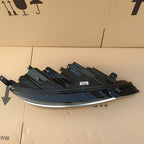 Sleek black automotive headlight assembly with chrome trim accents on a cardboard surface.