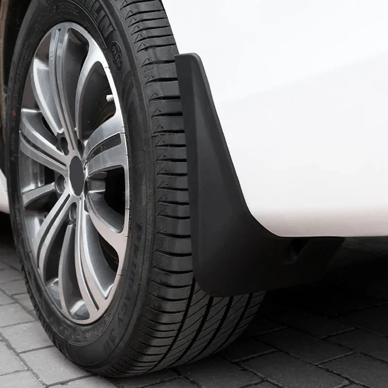 Close-up of a durable black matte plastic mud guard installed on a white car wheel arch.