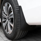 Close-up of a durable black matte plastic mud guard installed on a white car wheel arch.