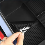 Hand peeling protective film from a black, ribbed waterproof car floor mat.