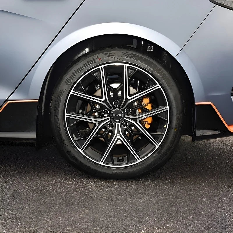 Close-up of a sleek black alloy wheel with silver accents and orange brake calipers on a grey car.