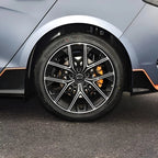 Close-up of a sleek black alloy wheel with silver accents and orange brake calipers on a grey car.