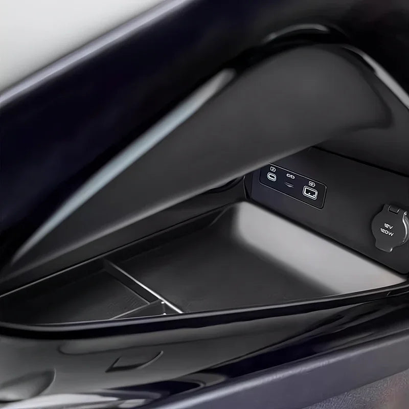 Close-up of a black glossy interior car storage compartment with a 12V power outlet.