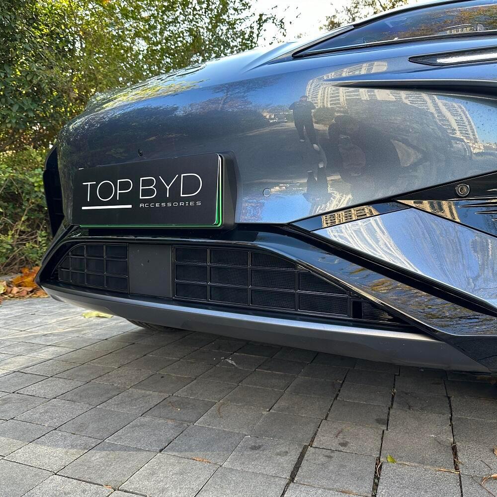 Black premium license plate frame with sleek white lettering on a grey BYD car bumper.