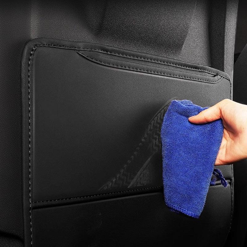 Hand cleaning a black waterproof leather car seat kick mat protector with a blue microfiber cloth.