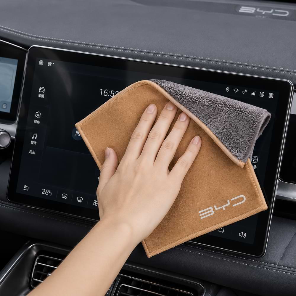 Person cleaning a car's touchscreen display with a BYD branded towel.