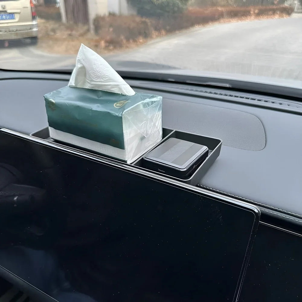 Black dashboard storage tray holding a green tissue box and a smartphone in a car interior.