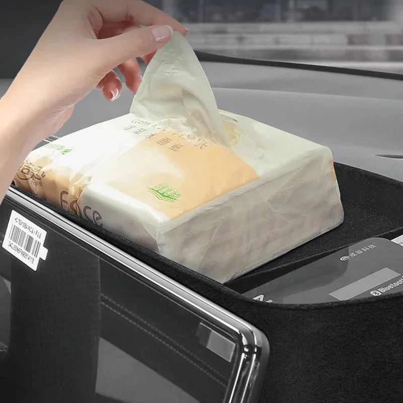 Hand pulling a tissue from a pack in a black velvet car dashboard storage organizer.