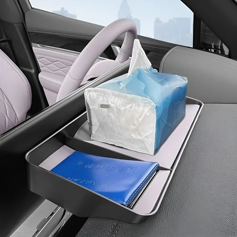 Black leather car seat organizer tray with a blue notebook and tissue box in a car interior.