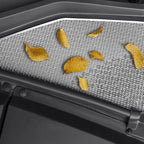Close-up of a grey textured car interior mat with scattered potato chips.