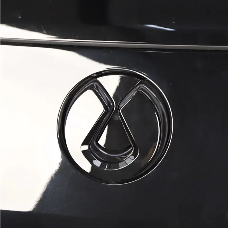 Glossy black metallic emblem featuring a sleek, modern geometric design on a dark car surface.