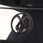 Glossy black metallic emblem featuring a sleek, modern geometric design on a dark car surface.