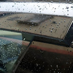 Water droplets on a sleek black car window and roof, showcasing a smooth, reflective finish.