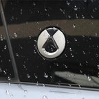 Close-up of a silver metallic car emblem on a glossy black surface with water droplets.