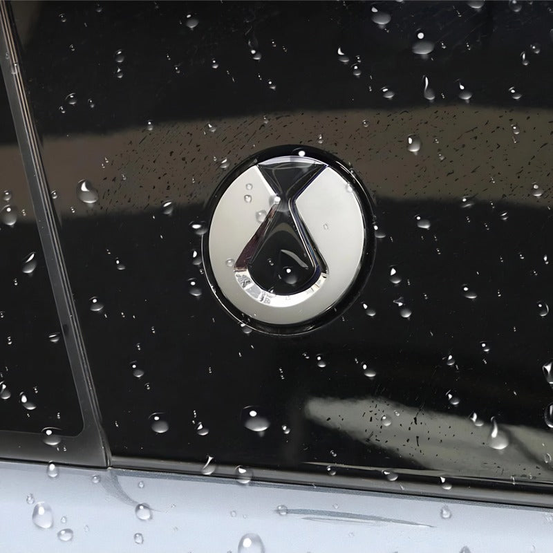 Close-up of a silver metallic car emblem on a glossy black surface with water droplets.