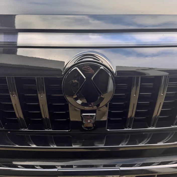 Close-up of a glossy black chrome front grille emblem for a luxury vehicle.