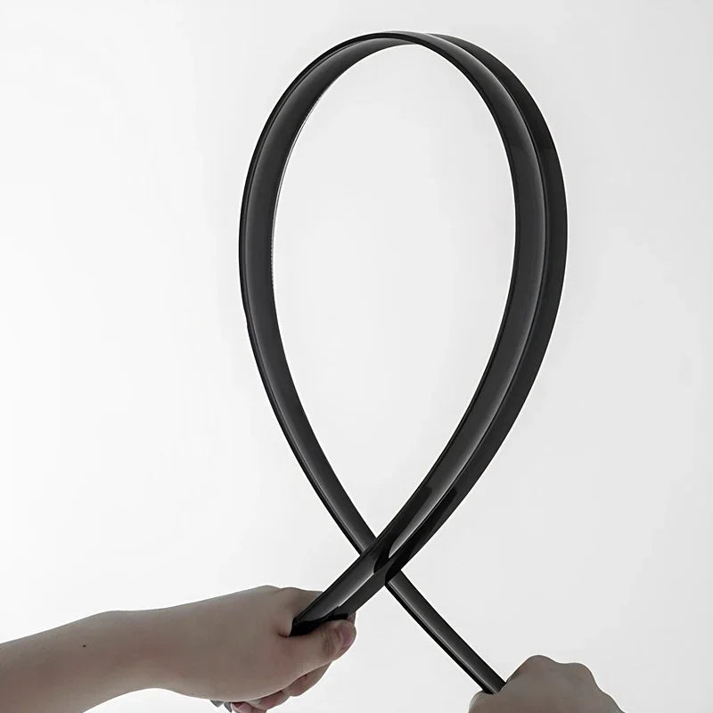 Hands holding a flexible, black rubberized protective strip for automotive use.