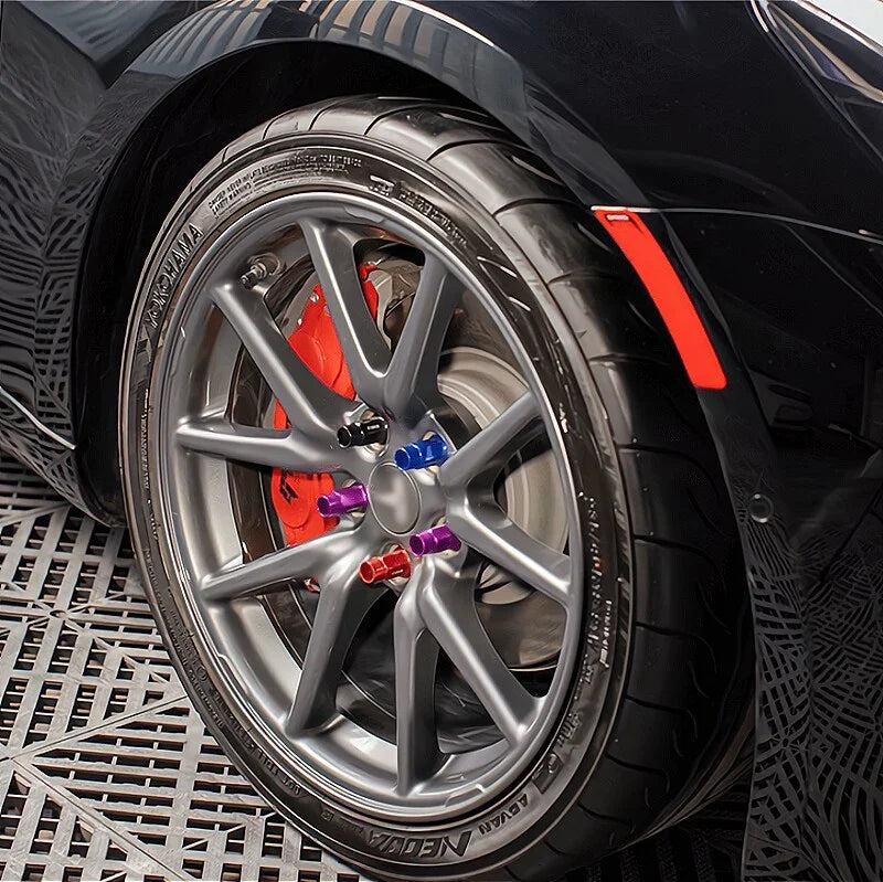 Close-up of grey alloy wheel with red brake calipers and multicolored anodized wheel lug nuts.