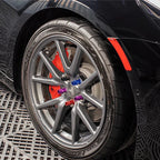 Close-up of grey alloy wheel with colorful anodized aluminum lug nuts and red brake calipers.