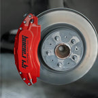 Red aluminum racing brake caliper cover installed on a silver car disc brake rotor.