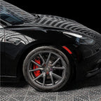 Glossy black car exterior featuring dark grey multi-spoke alloy wheels and red brake calipers.
