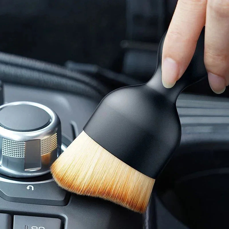 Black detailing brush with soft natural bristles cleaning a car interior console.
