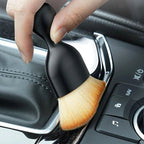 Black ergonomic car detailing brush with soft tan bristles cleaning vehicle interior trim.