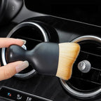 Black detailing brush with soft tan bristles cleaning car air vent vents.