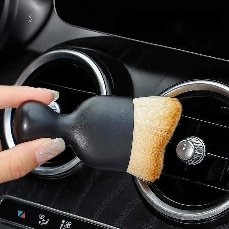 Black detailing brush with soft tan bristles cleaning car air vent vents.