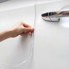 Hand applying a clear, transparent protective paint protection film to a white car door.