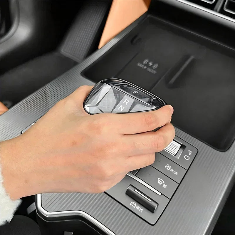 Hand holding a carbon fiber pattern gear shift knob in silver for BYD car interiors.
